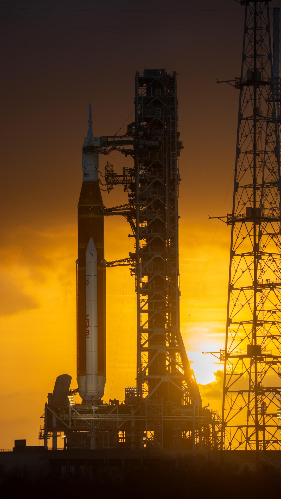 This image shows a sunset of NASA’s SLS (Space Launch System) and Orion spacecraft at NASA’s Kennedy Space Center. NASA's massive Crawler-Transporter, upgraded for the Artemis program, carried the powerful SLS rocket and Orion spacecraft on the Mobile Launcher from the Vehicle Assembly Building to Launch Pad 39B at Kennedy Space Center in preparation for the Artemis II mission.